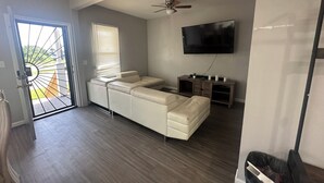 Un salon comprenant un canapé d’angle, un téléviseur fixé au mur et un ventilateur de plafond.