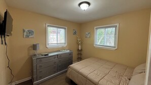 A bedroom with two windows, a dresser, a bed, and a ceiling light.
