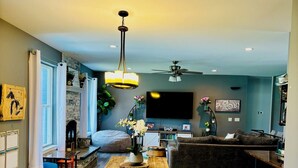 A modern living room with a wooden dining table, a sofa, and a TV mounted on the wall.