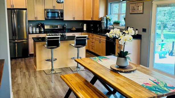 A modern kitchen with wooden cabinets, stainless steel appliances, and a wooden dining table with benches.