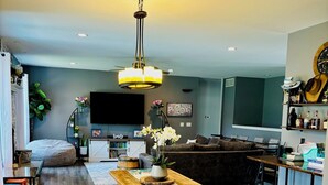 A modern living room with a wooden dining table, benches, a sofa, and a TV.