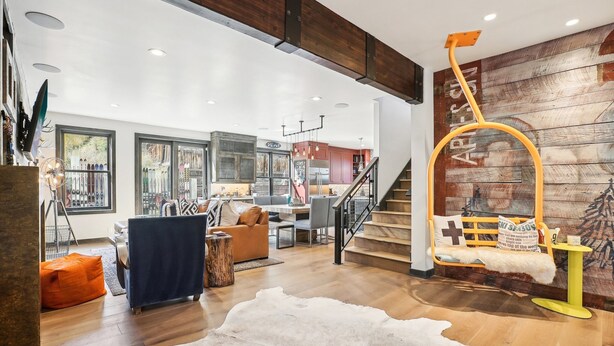 A spacious living area with a wooden floor, a sofa, a coffee table, and a staircase with a yellow railing.