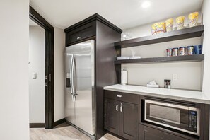 A modern kitchen with a stainless steel refrigerator, a microwave, and shelves with popcorn cans.