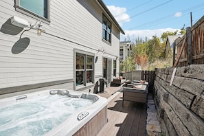 Un jacuzzi en una terraza de madera, una parrilla y mobiliario para exterior.