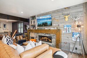 Una sala de estar acogedora con chimenea, sofá de cuero y varias decoraciones en las paredes, incluyendo una cabeza de ciervo y cuadros.