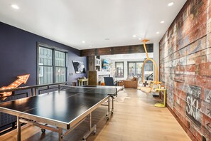 A ping pong table in a room with a wooden floor, a large window, and a rustic wall.