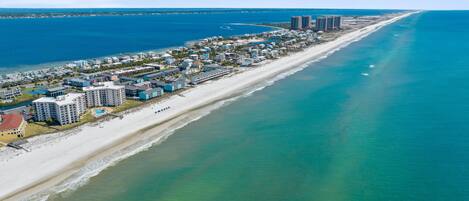 An aerial view of a coastal resort area with beachfront properties, a sandy beach, and a clear blue ocean.