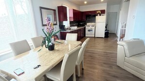 Un salón amplio con una mesa de comedor, sillas blancas, un ventilador de techo y una cocina al fondo.