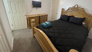 Un dormitorio con cama, cómoda, televisor y puerta.