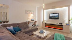 Ein modernes Wohnzimmer mit einer Couch, einem Couchtisch, einem Schreibtisch mit Computer, einem Kamin und einem an der Wand montierten Fernseher.