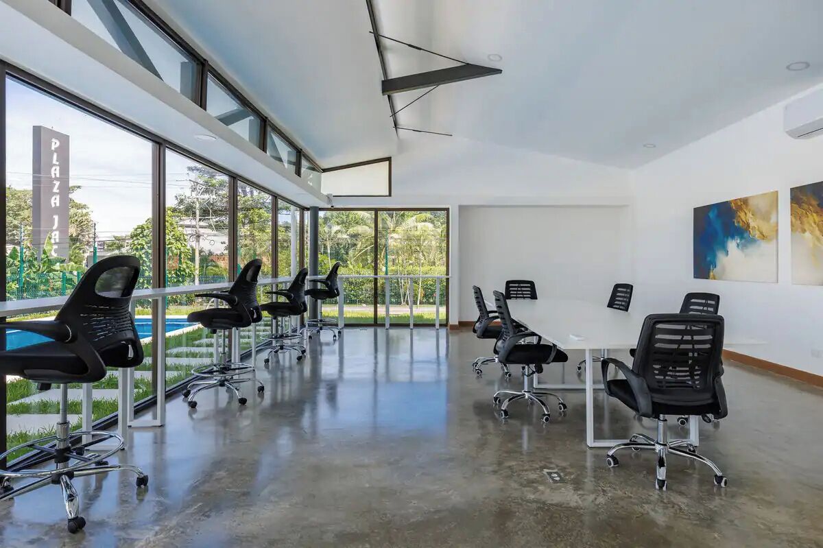 A modern conference room with large windows, black office chairs, and a white table.