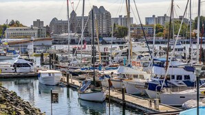 A marina with various boats docked, a cityscape in the background, and a sign indicating the marina's name. - Coastal Charm – Breathtaking Views with Work Desk by Victoria Prime! (Victoria)