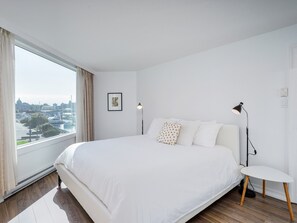 Un dormitorio moderno con una cama grande, vistas a la ciudad y una mesita de noche pequeña.
