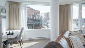 A modern living room with a leather sofa, a dining table with chairs, and large windows offering a view of the cityscape. - Coastal Charm – Breathtaking Views with Work Desk by Victoria Prime! (Victoria)