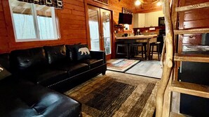 L’intérieur d’un chalet confortable, avec un canapé en cuir noir, une table à manger en bois et un coin cuisine.