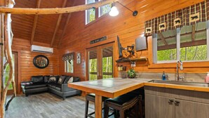 L’intérieur d’un chalet en bois comprend un coin repas, une cuisine et un salon avec un canapé et une cheminée.