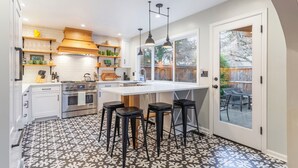 Una cocina moderna con una isla central, taburetes de bar y vistas al patio trasero a través de un ventanal.