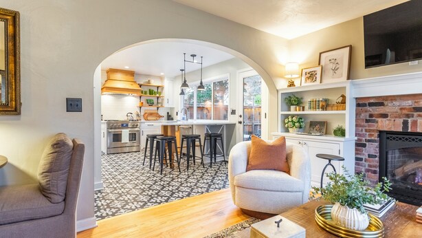 Una sala de estar moderna con un sofá, una mesa de centro y una chimenea. Se ve un área de cocina con una mesa de comedor y sillas a través de un arco.