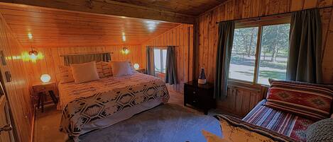 Ein gemütliches Schlafzimmer in einer Holzhütte mit einem großen Bett, einem Nachttisch und einem Fenster mit Vorhängen.