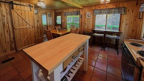 Un interior de madera con una mesa de comedor, sillas, una zona de cocina con estufa y ventanas que dan a zonas verdes.
