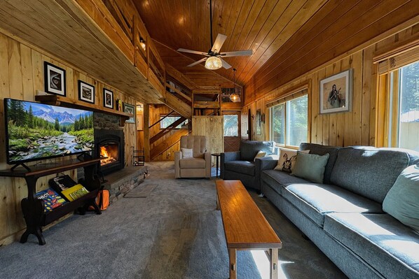 Un interior acogedor de cabaña con chimenea, televisor, sofá y ventilador de techo.