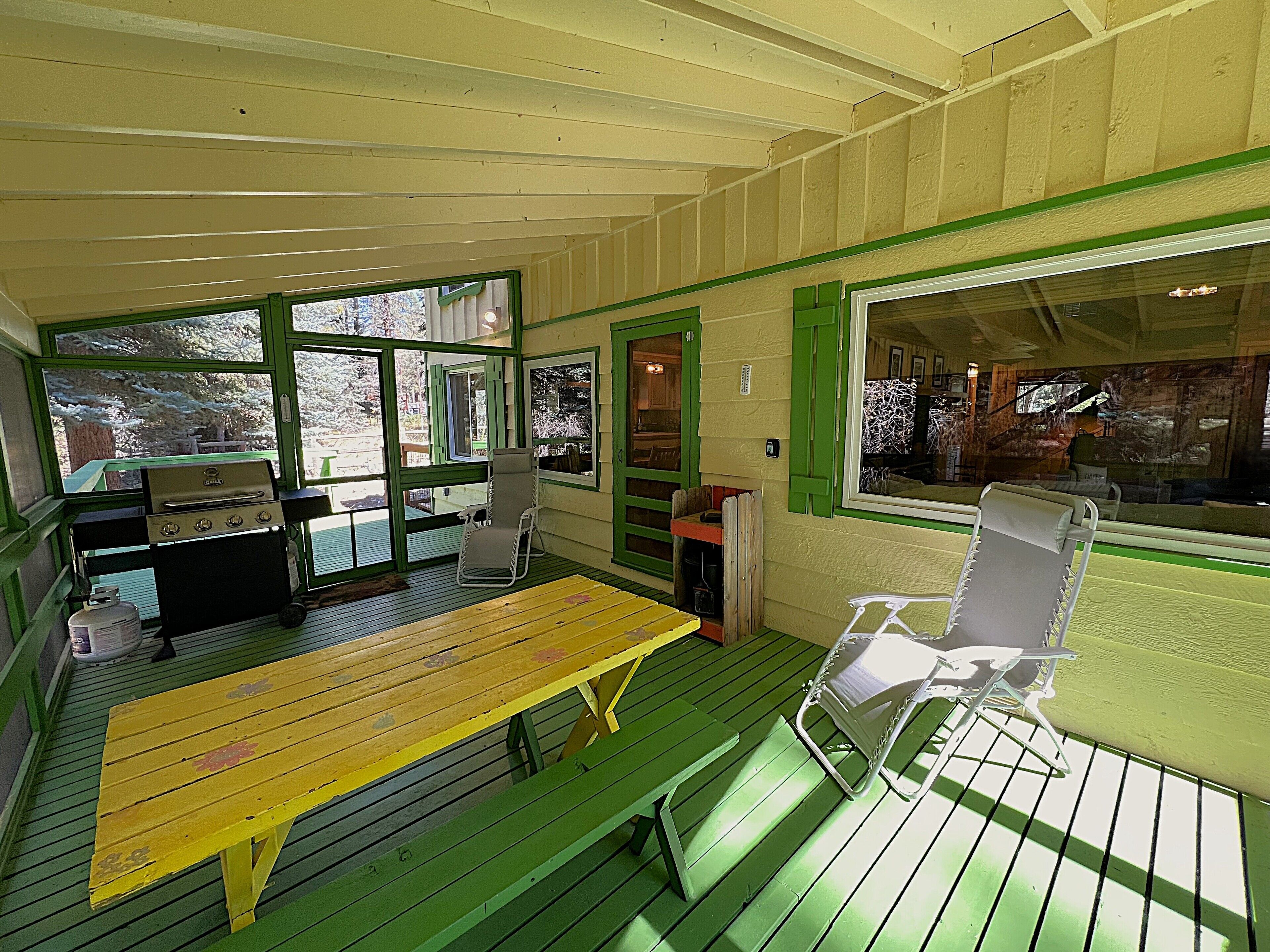 A covered outdoor area with a wooden table, chairs, and a grill.