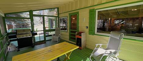 A covered outdoor area with a wooden table, chairs, and a grill.
