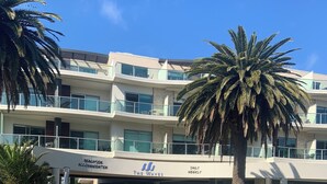 A multi-story hotel with a modern design, featuring a prominent entrance with a sign reading "Beachside Accommodation The Waves Daily Weekly."