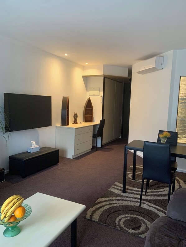 A modern living room with a flat-screen TV, a small dining area, and a cozy seating space.