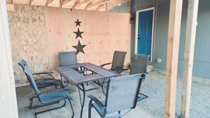 Ein Sitzbereich im Freien mit Tisch und vier Stühlen, einer Stern-Dekoration an der Wand und einer blauen Tür im Hintergrund.