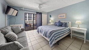 A bedroom with a bed, a couch, a TV, a ceiling fan, and a window. - Sugar Beach 110 - Bargain Bliss Studio (Orange Beach)