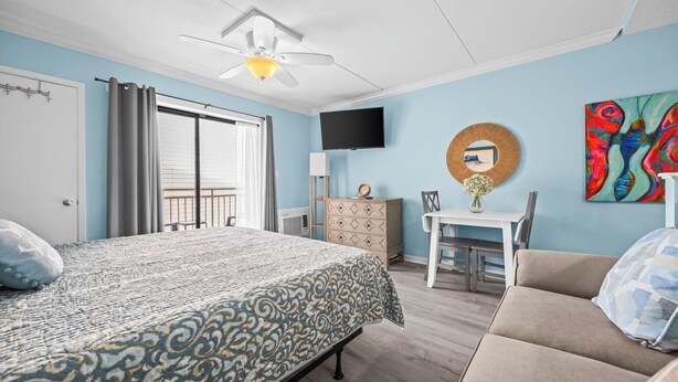 A bedroom with a bed, a desk, a chair, a TV, a dresser, and a painting on the wall. - Sugar Beach 135: Your Modern Coastal Studio (Orange Beach)