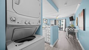 A laundry room with a front-loading washer and dryer, a sink, and a small kitchenette. - Sugar Beach 135: Your Modern Coastal Studio (Orange Beach)