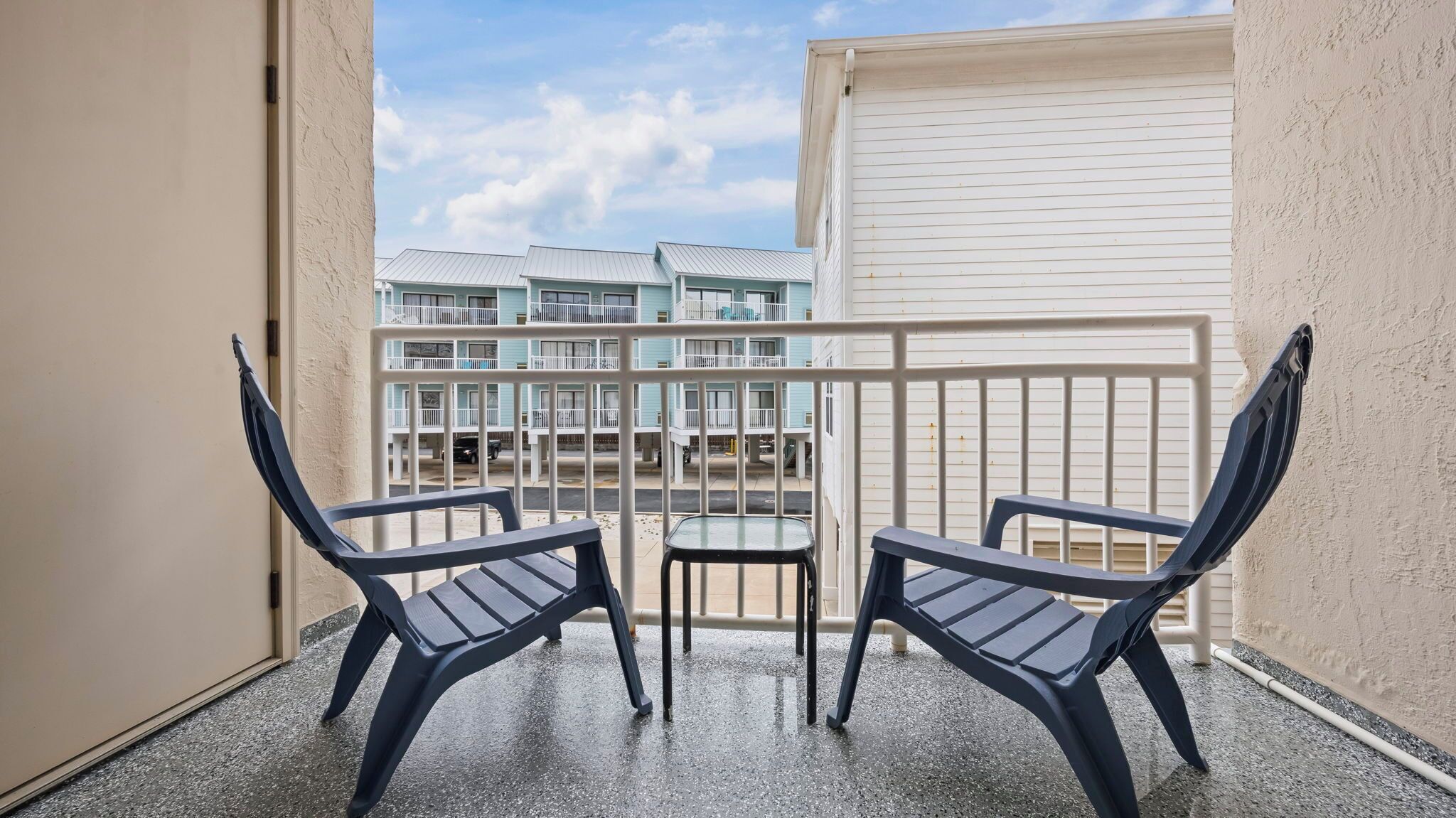 Ein Balkon mit zwei Stühlen und einem kleinen Tisch, mit Blick auf ein Gebäude mit mehreren Balkonen.