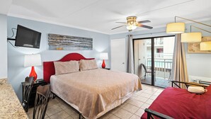 Una habitación de hotel con cama, televisión, ventilador de techo y balcón con vistas.