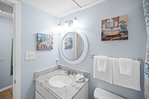 A bathroom with a marble sink, a round mirror, and two wall-mounted light fixtures. There are two framed pictures on the wall, and a towel rack with white towels. - Sugar Beach 160 Pool View (Orange Beach)