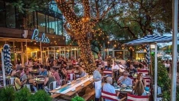 An outdoor dining area with tables and chairs, a large tree, and a building with a sign. - Relaxing Wellness Escape with Sauna & Cold Plunge (Austin)