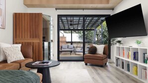 A modern living room with a sofa, armchair, coffee table, bookshelf, and a large TV. - Relaxing Wellness Escape with Sauna & Cold Plunge (Austin)