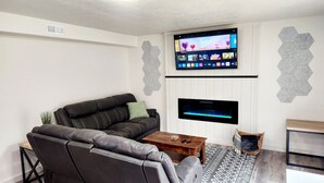 Ein modernes Wohnzimmer mit einer schwarzen Ledersofa, einem Holztisch, einem flachbildfernseher an der Wand und einem gemusterten Teppich.