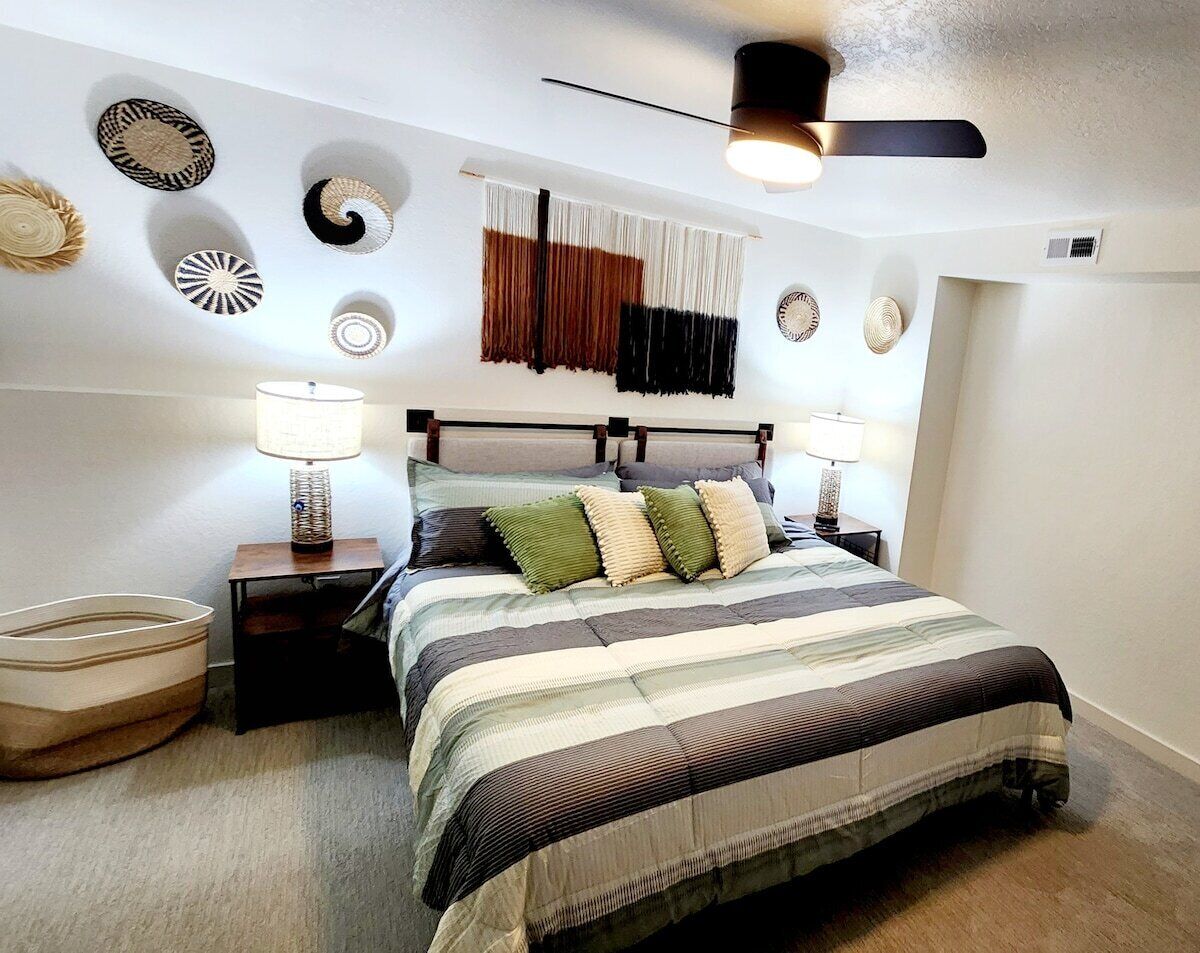 A bedroom with a bed, nightstands, a lamp, a ceiling fan, and wall decor.