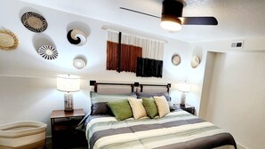 Ein Schlafzimmer mit Bett, Nachttischen, einer Lampe, einem Deckenventilator und Wanddekoration.