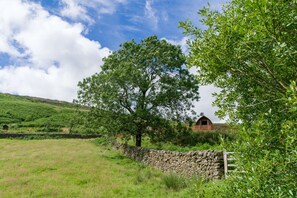 Un muro de piedra, un árbol grande y un edificio rojo en un paisaje rural.