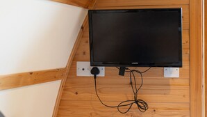 A room with a mounted flat-screen TV on a wooden wall, a bed with a patterned bedspread, and a remote control on the bed. - Cosy Rural Cabin With Hillside Viewpoint (Moffat)