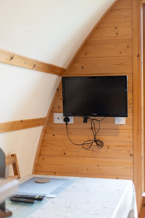 A room with a mounted flat-screen TV on a wooden wall, a bed with a patterned bedspread, and a remote control on the bed. - Cosy Rural Cabin With Hillside Viewpoint (Moffat)