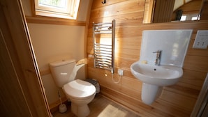 A compact wooden bathroom with a toilet, a sink, and a towel rack. - Cosy Rural Cabin in the Cornish Countryside (Helston)
