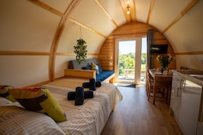 A cozy, compact room with a bed, a small seating area, a kitchenette, and a large window.