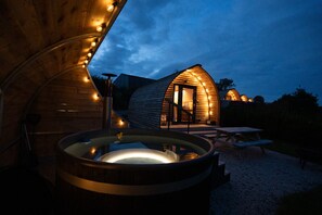 A wooden cabin with a curved roof, a hot tub, and a picnic table. - Cosy Cabin with Hot Tub in the Cornish Countryside (Helston)