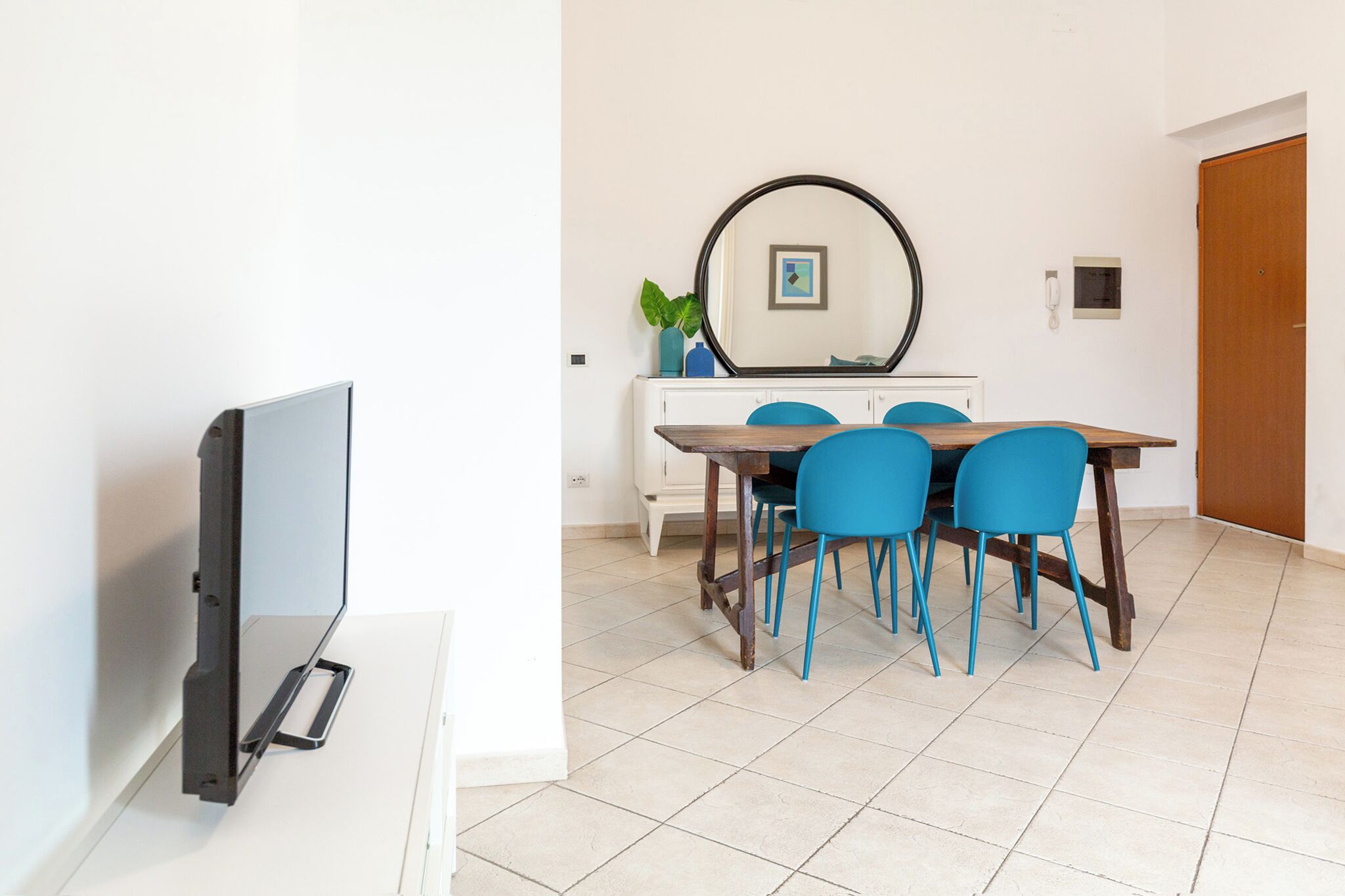 Un coin repas comprenant une table, des chaises, un téléviseur et un miroir au mur.