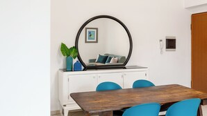 Ein Essbereich mit einem Holztisch und blauen Stühlen, einem weißen Schrank mit Spiegel und einer Pflanze darauf.