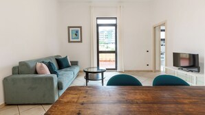 Ein Wohnzimmer mit grauem Sofa, einem Holztisch und einem Fernseher auf einem weißen Schrank.